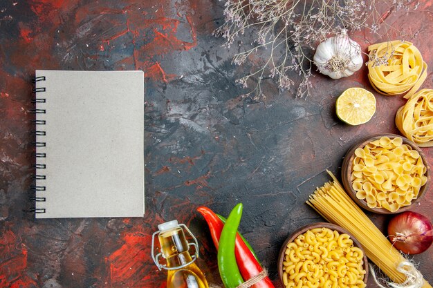 Gratis foto diner voorbereiding met ongekookte pasta's cayennepeper in elkaar gebonden met touw olie fles citroen knoflook en notitieboekje op gemengde kleurentafel