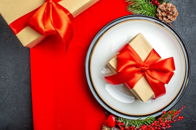 Dinerborden met cadeau erop en dennentakken met decoratieaccessoire coniferenkegel op een rood servet