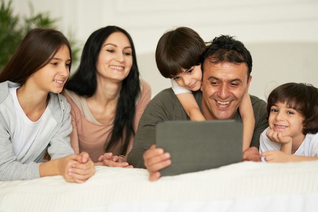 Dingen om thuis te doen gelukkige latijnse familie met schattige kleine kinderen met behulp van digitale tablet