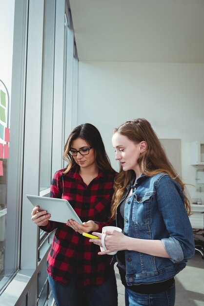 Directeuren die over digitale tablet bespreken terwijl het hebben van kop van koffie