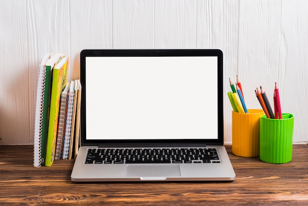 Divers type van boeken dichtbij laptop met het lege witte scherm op houten bureau