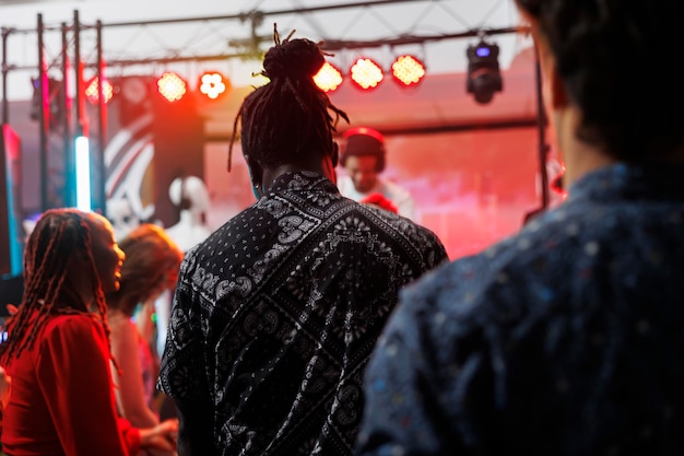 Gratis foto diverse clubbers feesten op de dansvloer tijdens het bijwonen van een elektronisch muziekconcert in een nachtclub. mensen dansen in de discotheek terwijl dj op het podium in de club optreedt