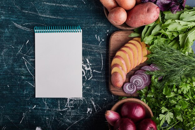 Diverse groenten geïsoleerd op blauwe tafel met een receptenboek opzij.