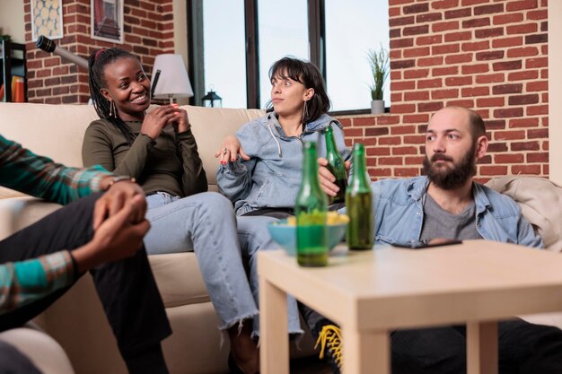 Diverse groep vrienden die lachen en een gesprek hebben tijdens het verzamelen van plezier, flessen bier drinken. Mensen hechten en praten over vrijetijdsbesteding, genieten van vriendschapsevenementen.