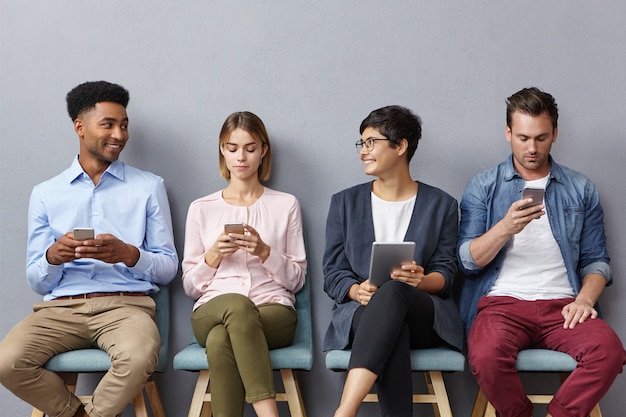 Diverse groepen jonge mensen hebben een levendig gesprek terwijl ze in de rij zitten, moderne gadgets gebruiken voor verschillende doelen