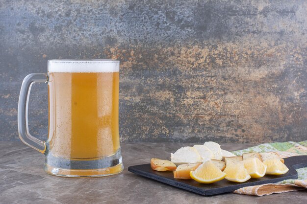 Diverse kaas en citroenplakken op donker bord met bier