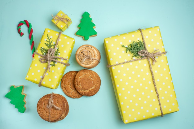 Diverse kerstboomsuikerkoekjes en gele geschenkdoos op pastelblauwe achtergrond