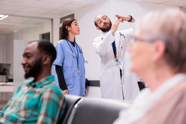 Diverse medische staf praten over gezondheidszorg bij de receptie van het ziekenhuis, discussiëren over patiënten en afspraken in de lobby van de medische faciliteit. Arts en verpleegster in wachtkamergebied.