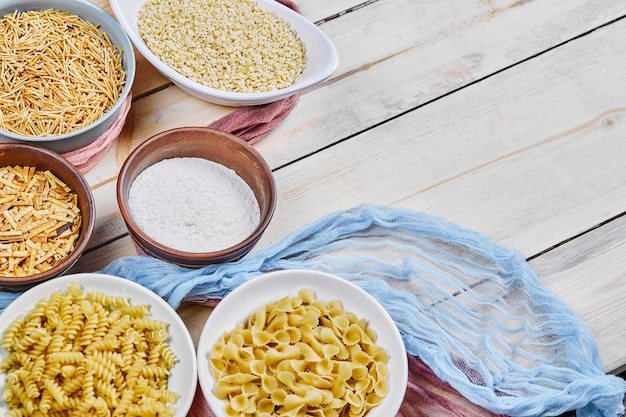 Diverse ongekookte pastakommen op houten tafel met blauw tafelkleed.