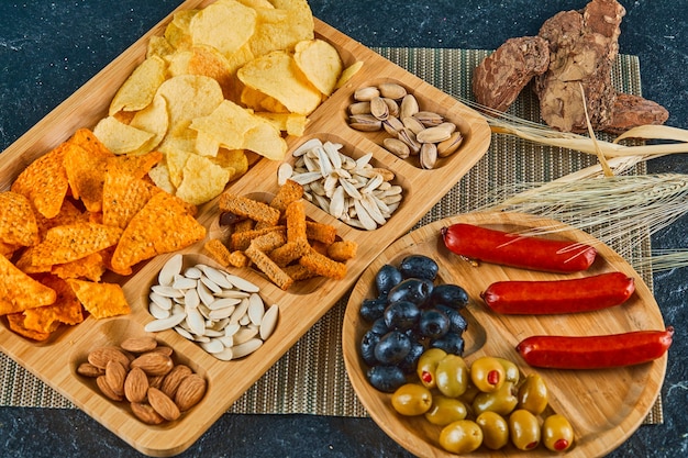 Diverse snacks, een bord worst, kaviaar en olijven op een houten tafel.