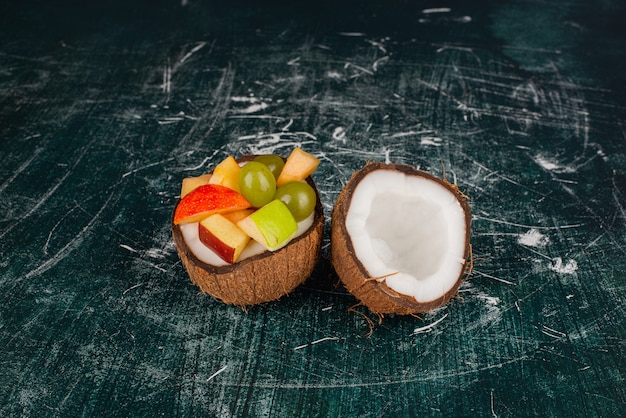 Diverse vruchten in half gesneden kokosnoot op marmeren tafel.