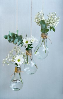 Diverse witte bloemen in vazen in de vorm van gloeilampen opgehangen aan touwtjes