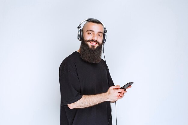 Dj met baard die een koptelefoon draagt en muziek van zijn afspeellijst op zijn smartphone zet.