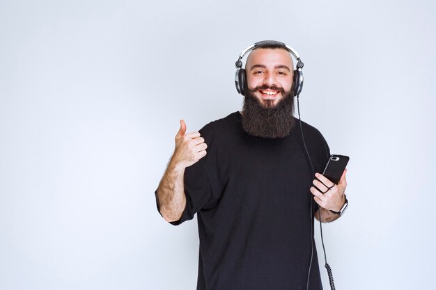 Dj met baard die koptelefoon draagt en geniet van de afspeellijst op zijn telefoon.