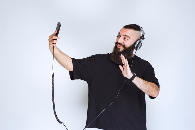 Dj met baard met koptelefoon die smartphonecamera opent en zijn selfie neemt.