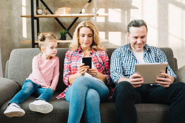 Dochter die ouders bekijkt die digitale tablet en mobiele telefoon thuis met behulp van