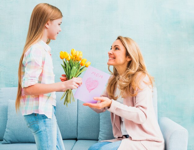 Dochter die tulpen en prentbriefkaar voor moeder voorstelt