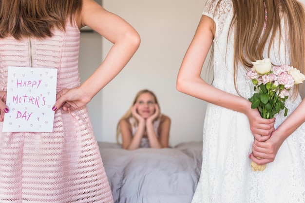 Dochters die wenskaart en bloemen voor moeder houden