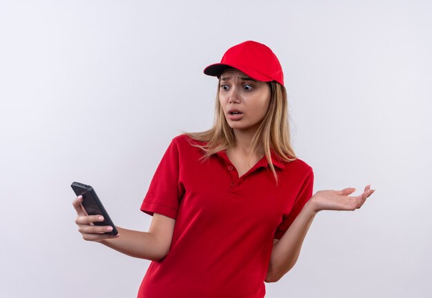 Doen schrikken jong leveringsmeisje die rood uniform en GLB dragen die en telefoon bekijken die op wit wordt geïsoleerd