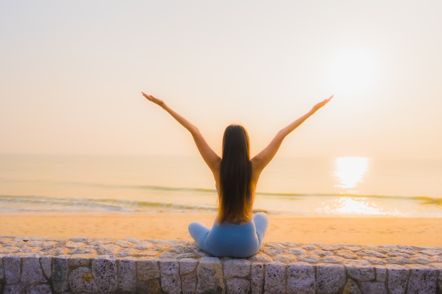 Doet de portret jonge Aziatische vrouw meditatie rond overzeese strandoceaan bij zonsopgang