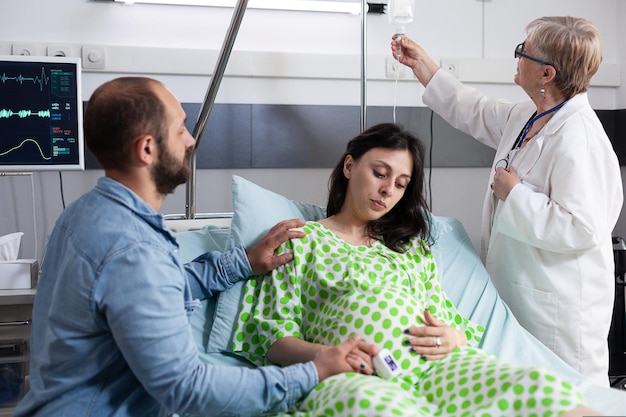 Dokter controleert de gezondheidszorg van de zwangere vrouw in de ziekenhuisafdeling met de vader van het kind dat de hand ondersteunt en vasthoudt. paar verwacht baby die onderzoek krijgt van verloskundige tijdens kraamtijd