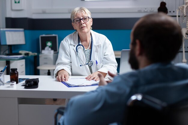 Dokter die advies geeft aan man die in een rolstoel zit bij controlebezoek. Huisartsgesprek met patiënt met een handicap op consultatieafspraak. Mensen praten in de kast