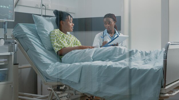 Dokter doet overleg met jonge patiënt in ziekenhuisafdeling. Huisarts in gesprek met zieke vrouw om ziektediagnose en gezondheidszorgbehandeling voor medisch herstel te onderzoeken.