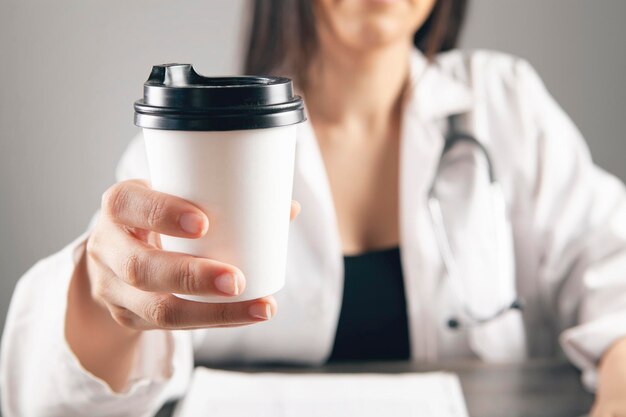 Dokter houdt koffie voor werktafel Premium Foto