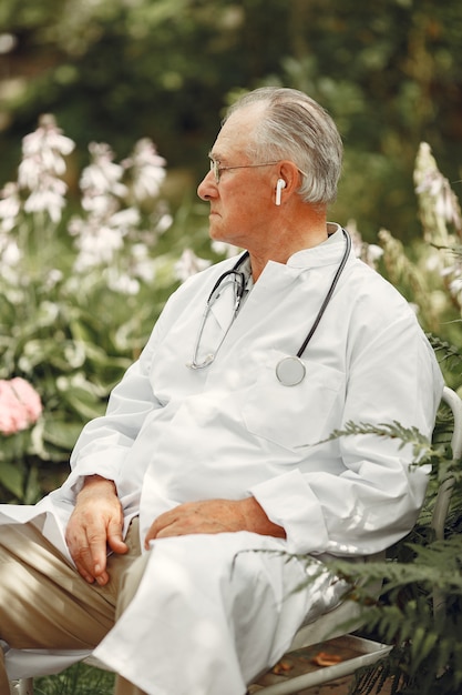 Dokter in een wit uniform. Oude man zit in een zomerpark. Oudste met een stethoscoop.