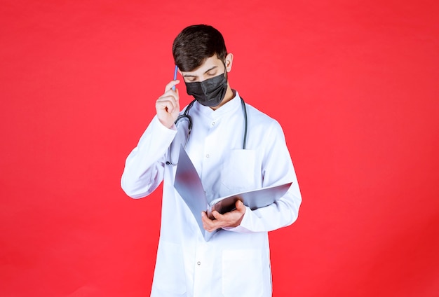 Dokter in zwart masker denken en maken van aantekeningen op zwarte map.