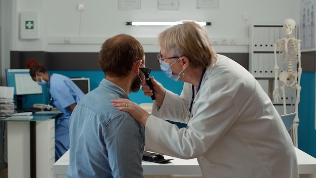 Dokter-otoloog onderzoekt oorontsteking van patiënt met otoscoop tijdens covid 19 pandemie. Gezondheidsspecialist die otologieinstrument gebruikt om overleg te doen bij de afspraak van het controlebezoek.