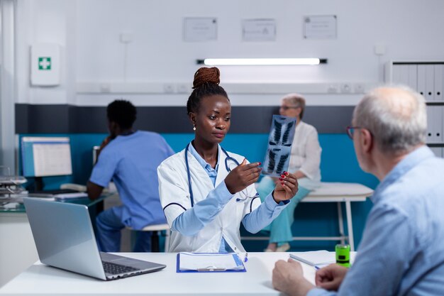 Dokter van Afro-Amerikaanse etniciteit met röntgenfoto voor oude patiënt