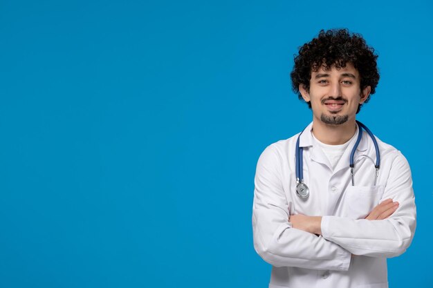 Doktersdag gekrulde knappe schattige kerel in medisch uniform die handen vol vertrouwen kruist