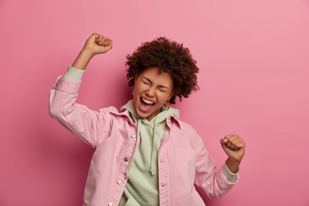 Dolblij Afro-Amerikaanse student maakt overwinningsdans, roept blij uit, is in de wolken, behaalt succes, draagt hoodie met jasje