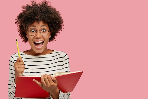 Dolblij zwarte vrouw houdt leerboek en potlood vast, roept met verbazing uit
