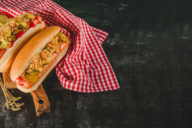 Gratis foto donker oppervlak met tafelkleed en twee heerlijke hotdogs