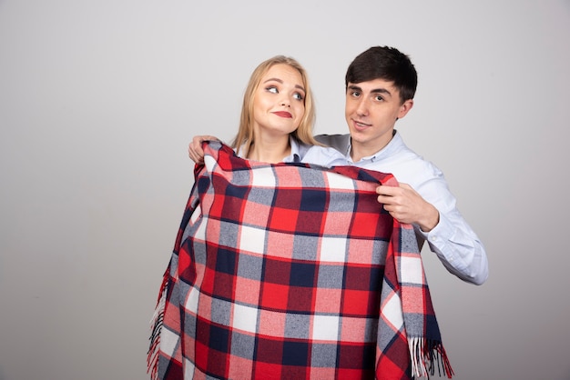 Donkerbruin manmodel dat geruite deken bedekt met blonde vrouw