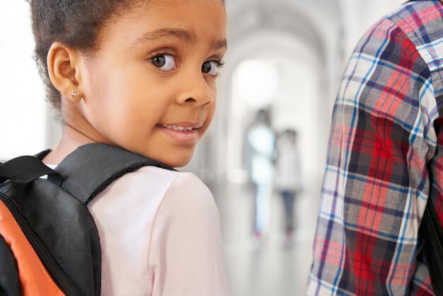 Gratis foto donkerbruin schoolmeisje die camera over schouder bekijken