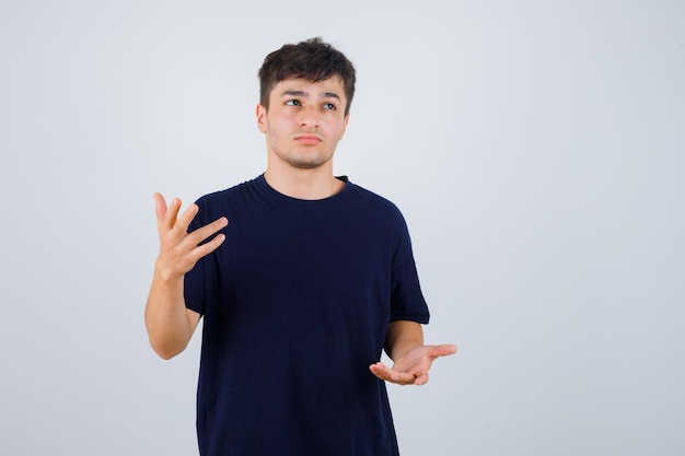 Donkerbruine man die doet alsof hij iets in een t-shirt laat zien en er attent uitziet. vooraanzicht.