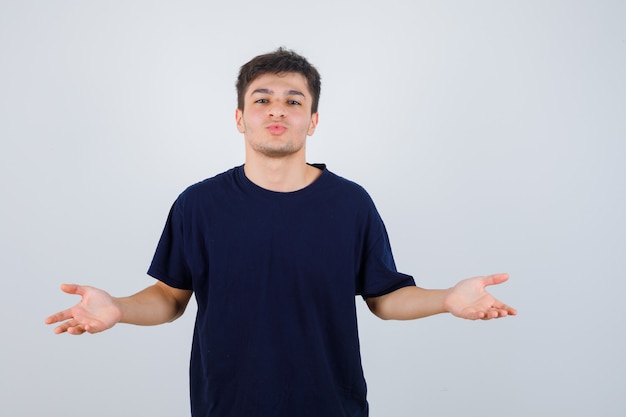 Donkerbruine man die handpalmen opzij in t-shirt spreidt en vreugdevol, vooraanzicht kijkt.