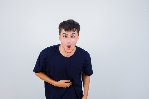 Donkerbruine man in donkere t-shirt die hand op buik houdt en wrokkig, vooraanzicht kijkt.