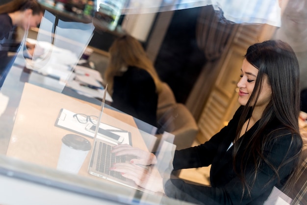 Donkerbruine onderneemster door een venster met laptop