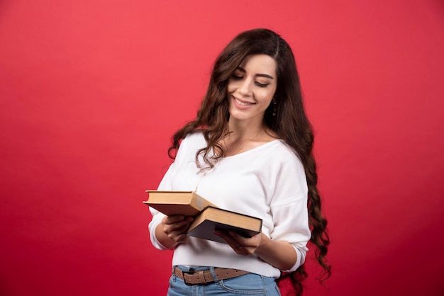 Donkerbruine vrouw die boeken op rode achtergrond bekijkt. Hoge kwaliteit foto