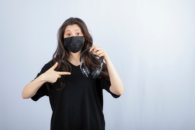 Donkerbruine vrouw met lang haar in medisch masker dat op hoofdtelefoons richt.