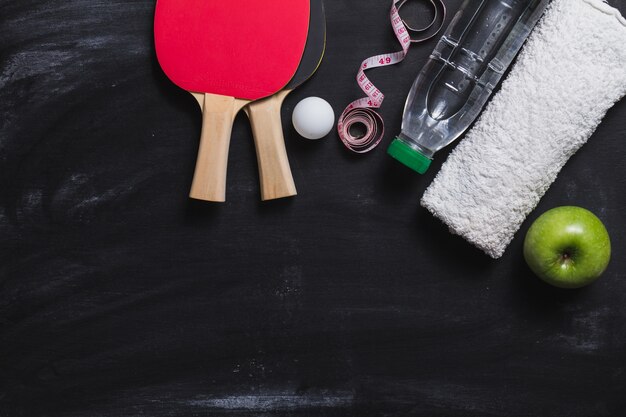 Donkere oppervlakte met ping pong rackets, een fles water en appel