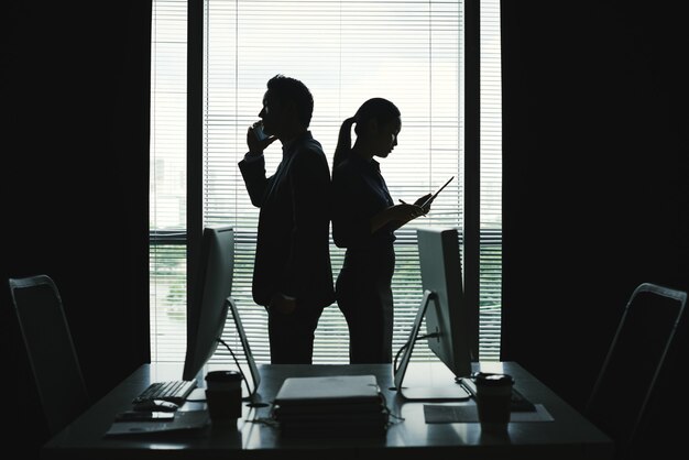 Donkere silhouetten van man en vrouw in bedrijfskledij die zich tegen venster in bureau bevinden