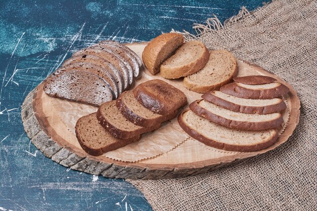 Donkere sneetjes brood op een houten bord op blauwe tafel.