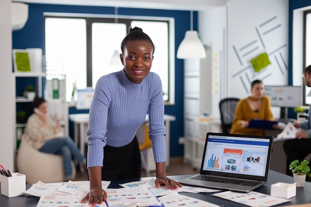 Donkere vrouw en collega's in het startbureau van het bedrijf werken om het project af te ronden. Divers team van zakenmensen die financiële bedrijfsrapporten van de computer analyseren.