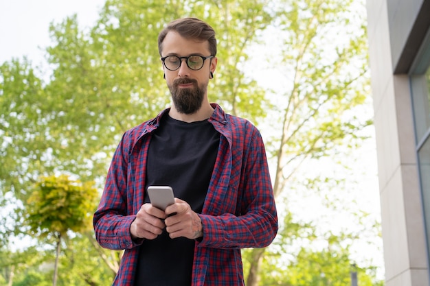 Donkerharige man in ronde bril met smartphone op straat