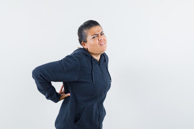 Donkerharige vrouw die aan nekpijn in jas lijdt en ongemakkelijk kijkt. vooraanzicht.